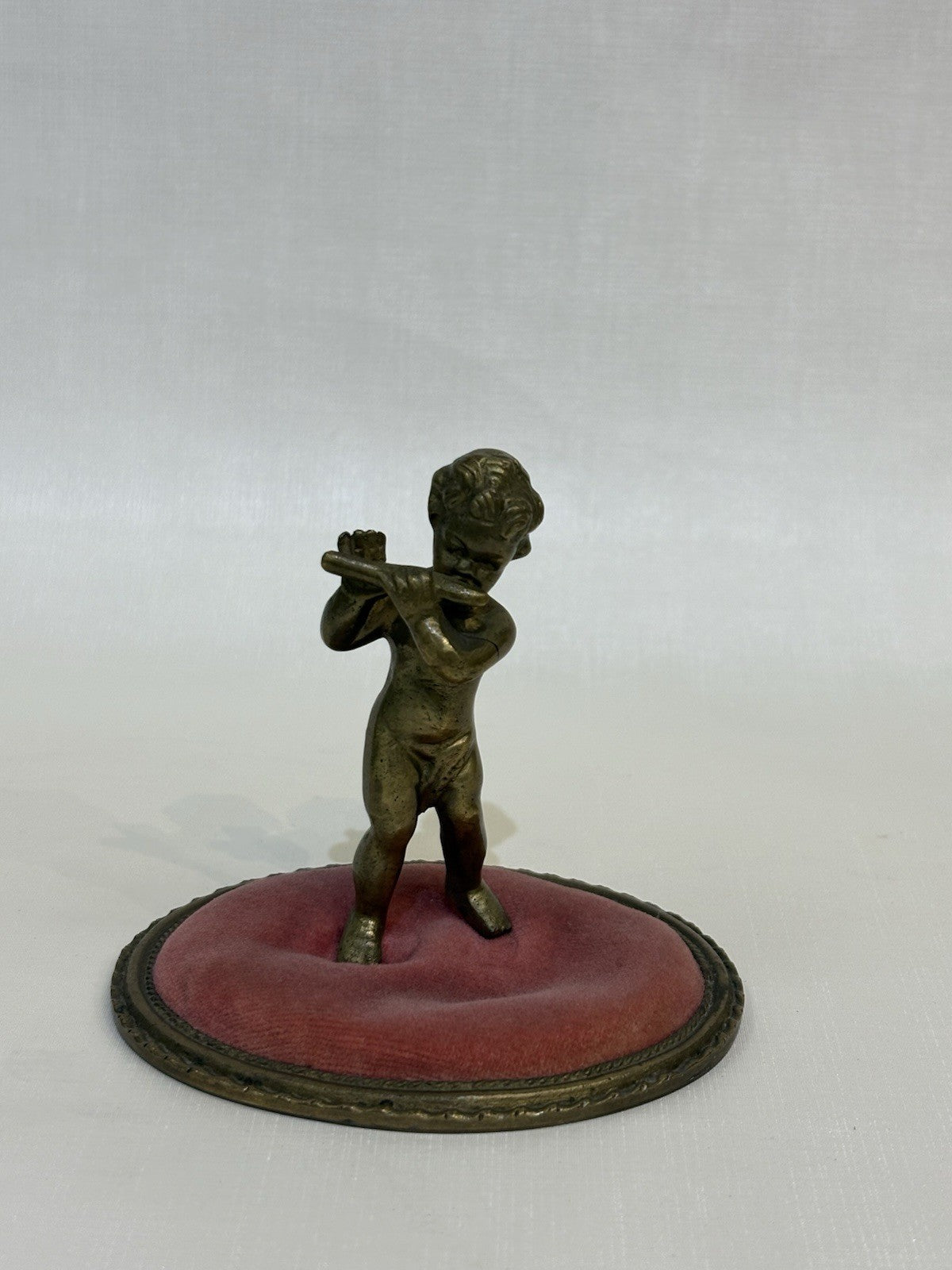 ntique pincushion featuring a small bronze figure of a child playing a flute