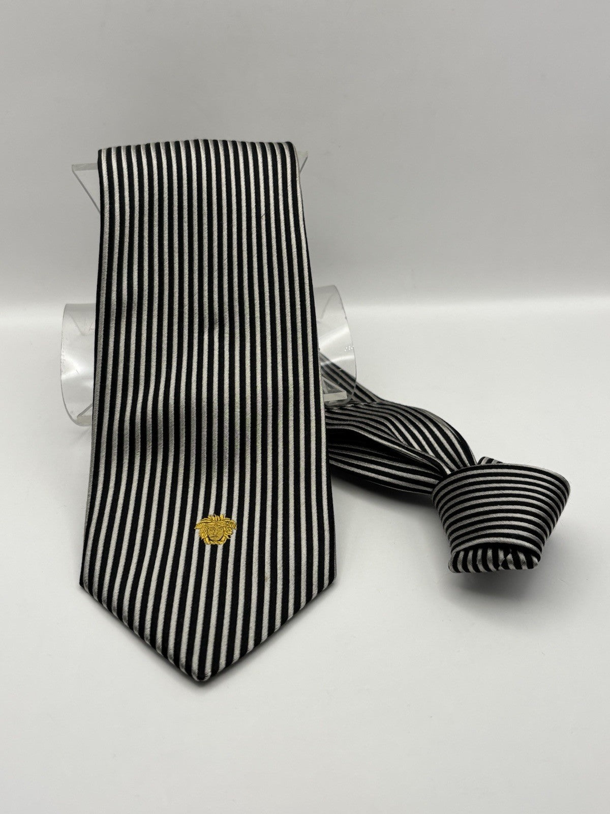 Versace necktie refined black and silver striped pattern by a gold Medusa logo.