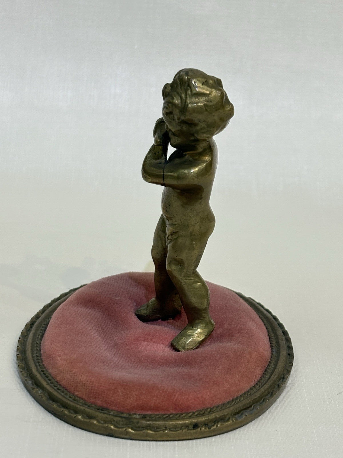 ntique pincushion featuring a small bronze figure of a child playing a flute