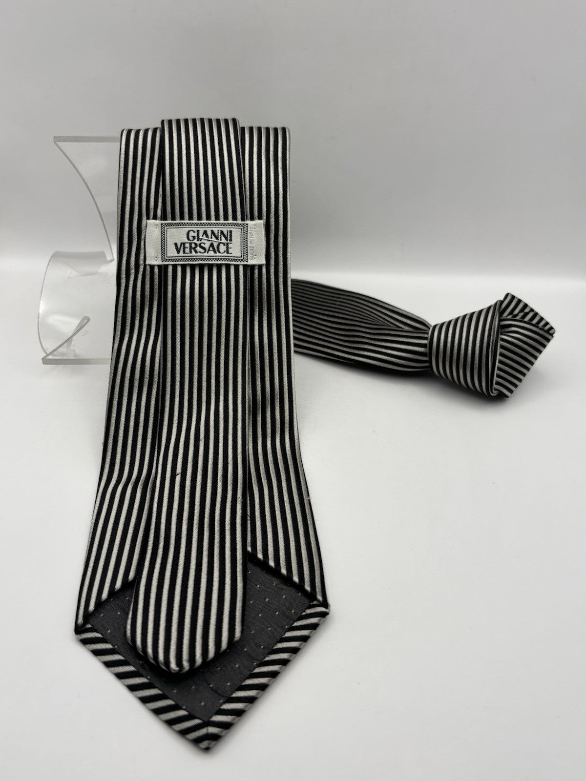 Versace necktie refined black and silver striped pattern by a gold Medusa logo.
