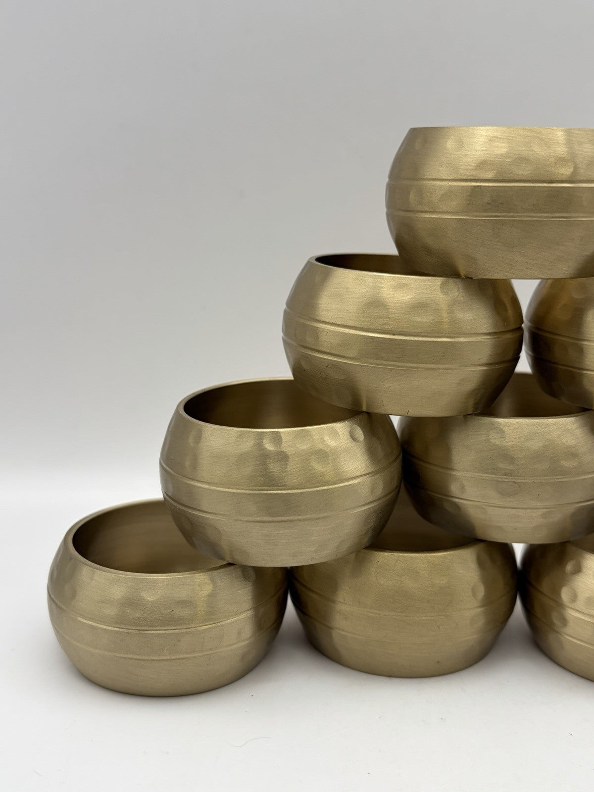 vintage or late 20th-century hammered brass napkin rings, often sold in sets.