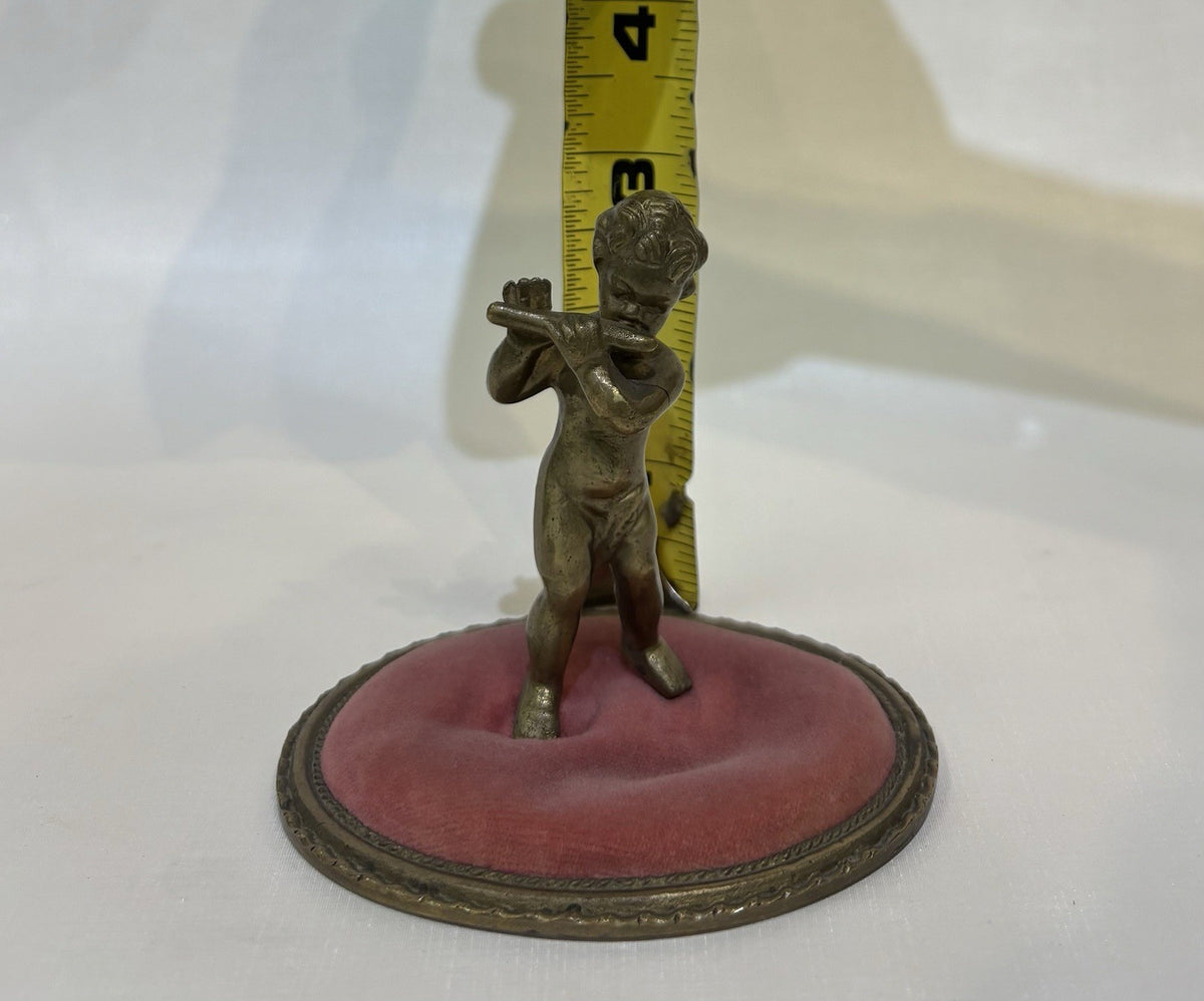 ntique pincushion featuring a small bronze figure of a child playing a flute