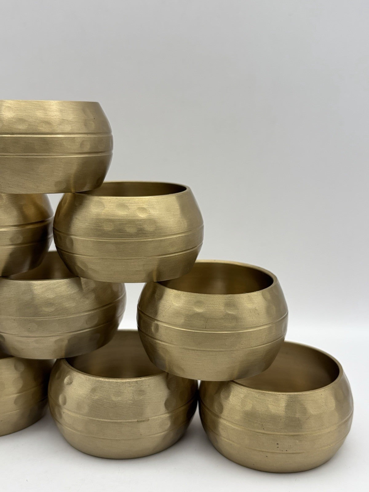 vintage or late 20th-century hammered brass napkin rings, often sold in sets.